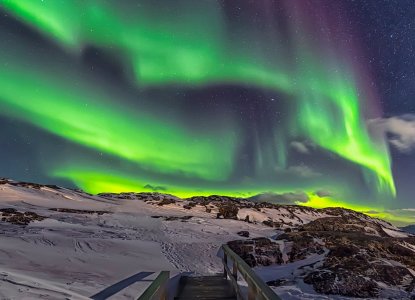 Snow and rocky covered  in the dark with bright green Northern Lights (Aurora Borealis)  in the sky in Illulissat Greenland