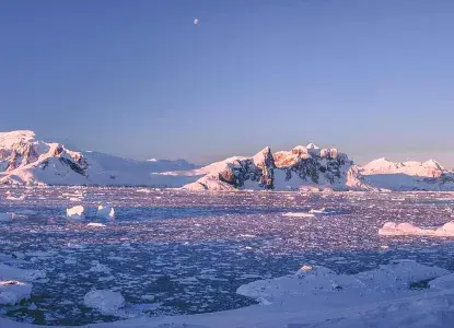 snowy Antarctic mountains and brash ice covering bay at sunrise