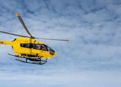 Quark yellow Flightseeing helicopter in the clear blue sky with few clouds in Antarctica with photo by Michelle Sole