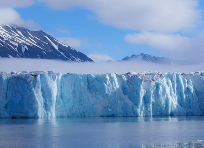 Large Glacier in Svalbard with mountains in the background and calm waters in foreground