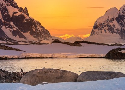 Calm bay in Antarctica with midnight sun colouring snowy mountain